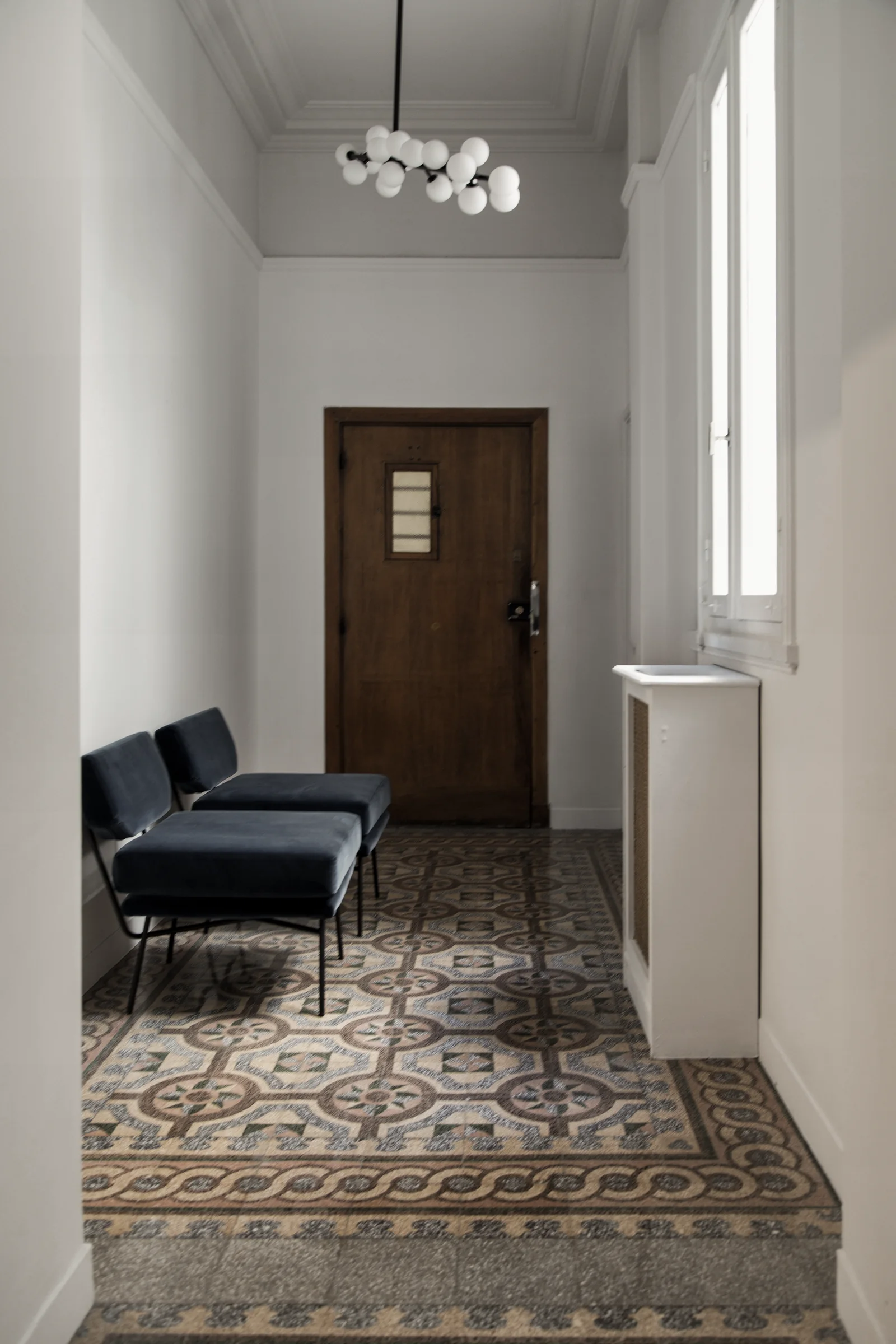 Bombyx — Restored tiled entrance hall with blue chairs and a pendant light