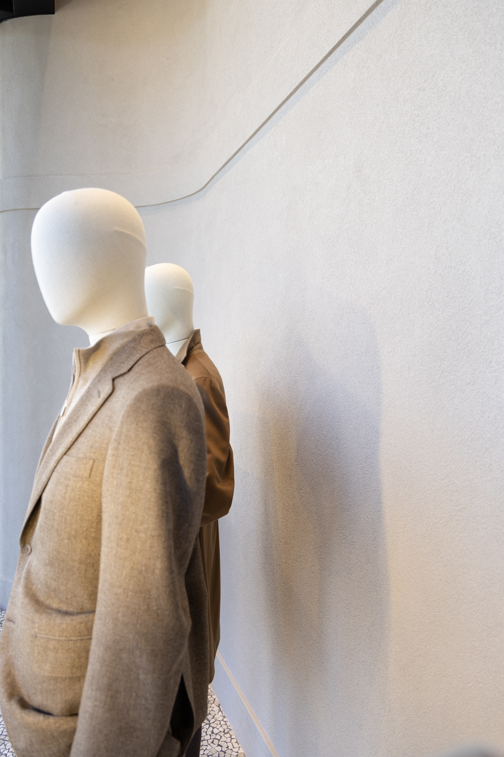 Incrocio Glyfada — Two mannequins and their shadows against a curved textured plaster wall